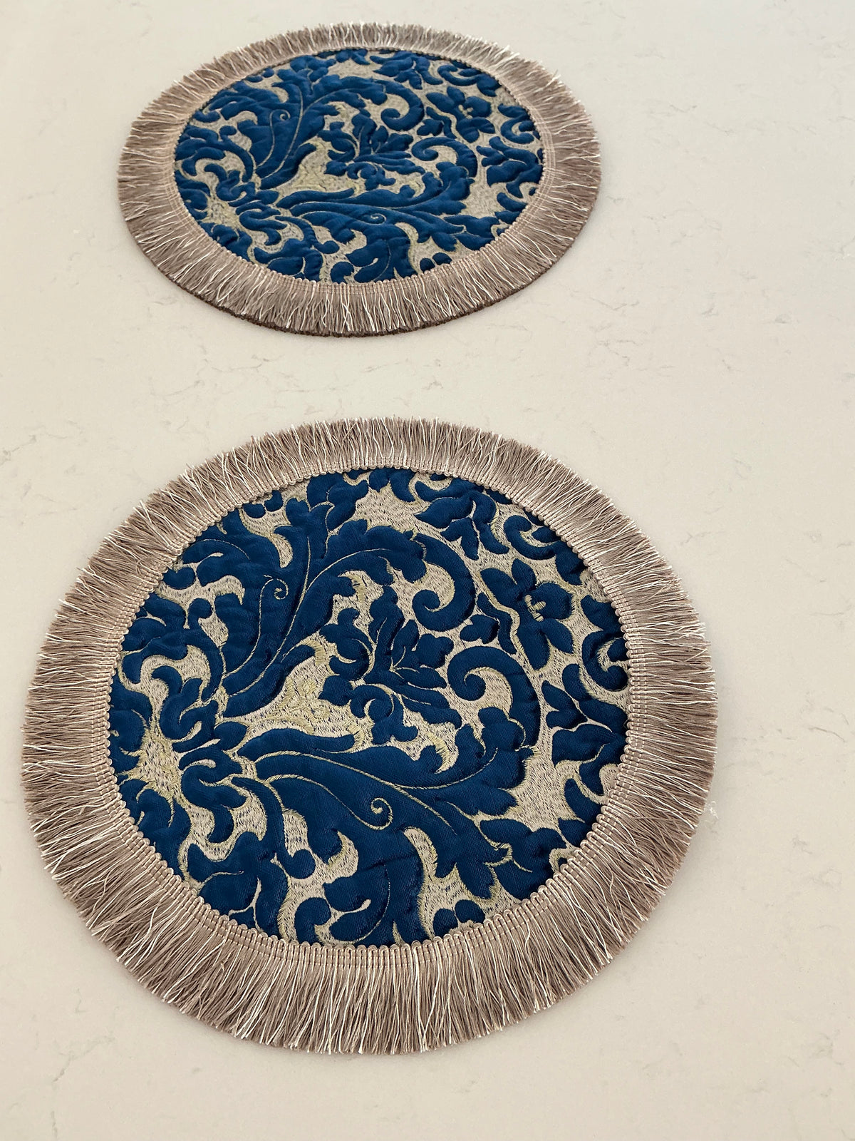 Ornate round table topper in navy and silver jacquard with tassel fringe border, flat lay