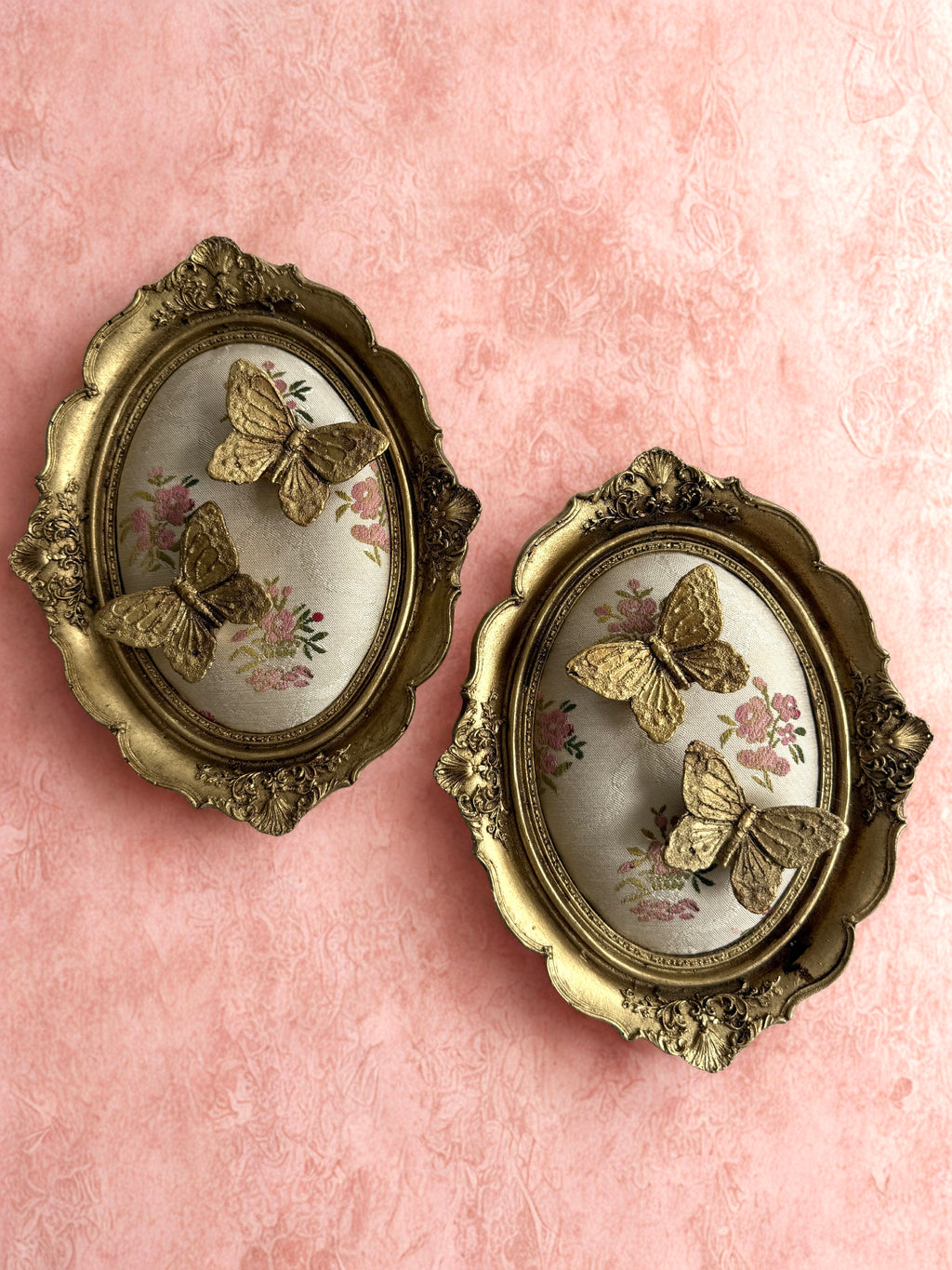 Set of two ornate gold oval butterfly wall frames on pink background