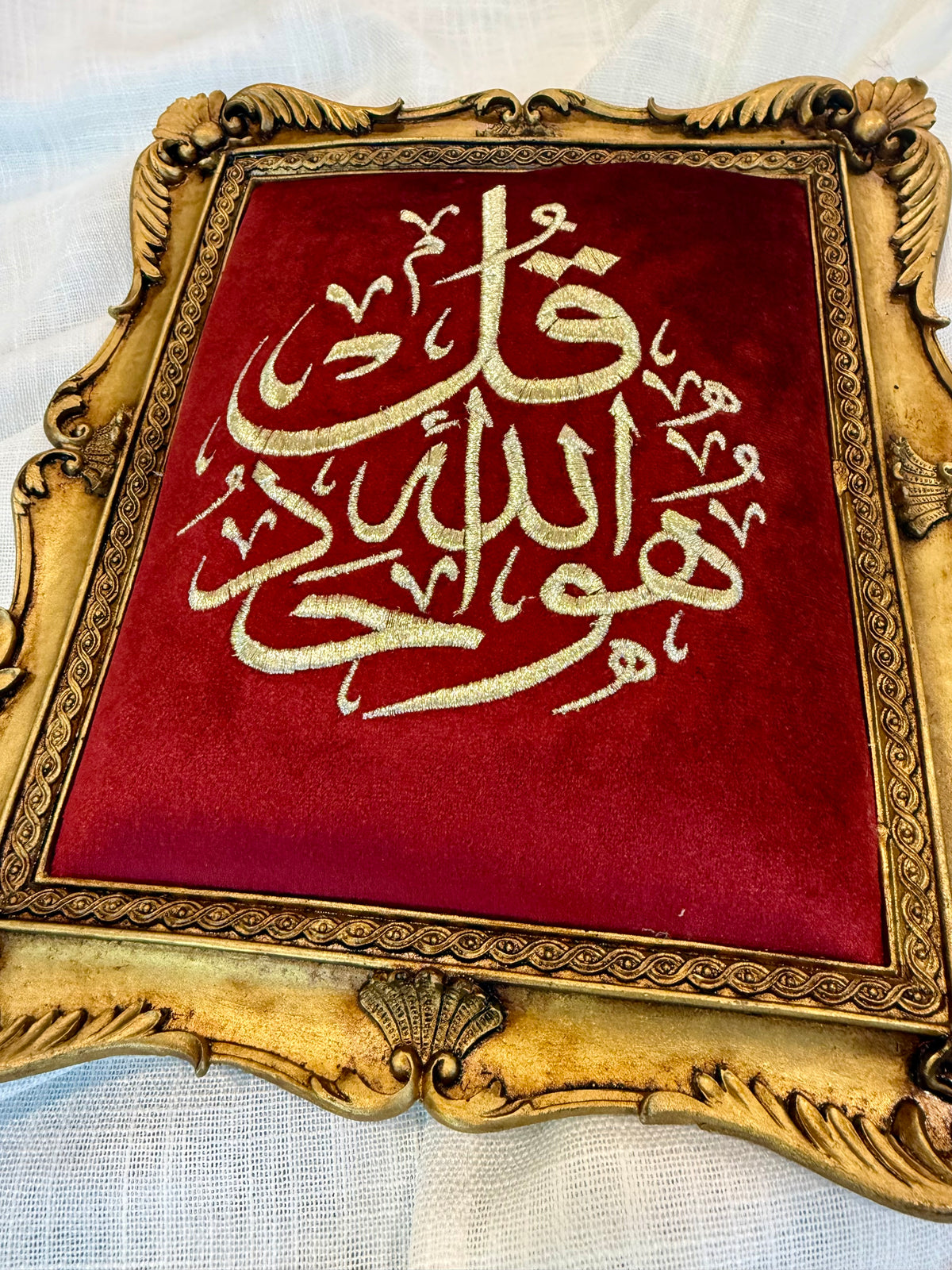 Decorative framed Islamic wall art featuring gold Arabic calligraphy on a burgundy background